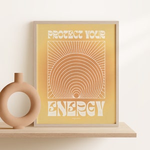 以下が含まれることがあります： 黄色の背景に白い文字で「Protect Your Energy」と書かれた額装されたプリント。文字はレトロなフォントスタイル。背景には、同心円状の円を持つスタイリッシュな太陽が描かれている。