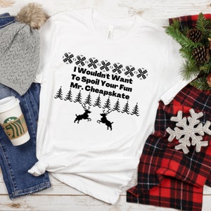 May include: White t-shirt with a black Christmas-themed design. The design features a row of snowflakes, a row of pine trees, and two reindeer. The text reads "I Wouldn't Want To Spoil Your Fun Mr. Cheapskate".
