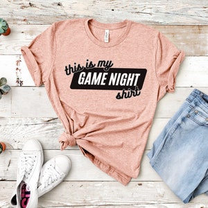 May include: A peach-colored t-shirt with the text "This is my GAME NIGHT shirt" in black lettering.