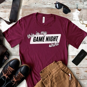 May include: Burgundy t-shirt with the text "This is my GAME NIGHT shirt" in white lettering with a black outline.