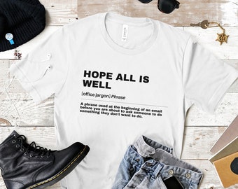 May include: White t-shirt with black text that reads "HOPE ALL IS WELL [office jargon] Phrase A phrase used at the beginning of an email before you are about to ask someone to do something they don't want to do."