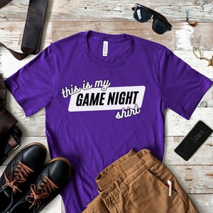 May include: Purple t-shirt with white text that says "This is my GAME NIGHT shirt".