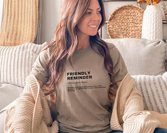 May include: A woman wearing a brown t-shirt with the text "FRIENDLY REMINDER [office jargon] Phrase There's nothing friendly about this. This phrase is a signal that it's your last and final warning." printed on it.