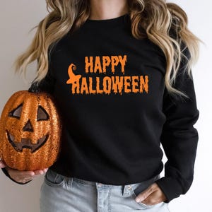 Puede incluir: Sudadera negra con texto naranja que dice "Happy Halloween" con un gráfico de sombrero de bruja.
