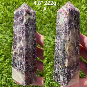 May include: A purple and white Lepidolite crystal point, also known as a wand, measuring 4.8 inches and weighing 222 grams. The crystal has a unique, speckled pattern and is a popular choice for crystal healing.