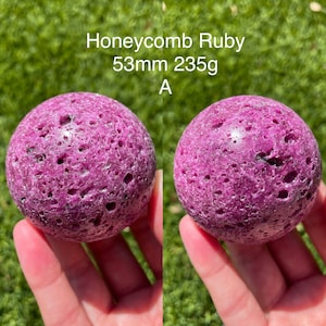 May include: A close-up of a honeycomb ruby sphere, measuring 53mm and weighing 235g. The sphere is a deep pink color with a textured surface.