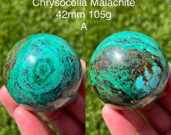 May include: A 42mm, 105g Chrysocolla Malachite sphere with green, blue, and brown swirling patterns. The sphere is being held in a hand.