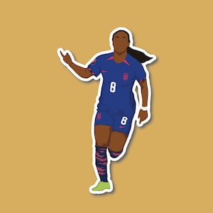May include: A female soccer player wearing a blue jersey with the number 8 on it. She is wearing black and white striped socks and black cleats. She is celebrating a goal with her arm raised in the air.