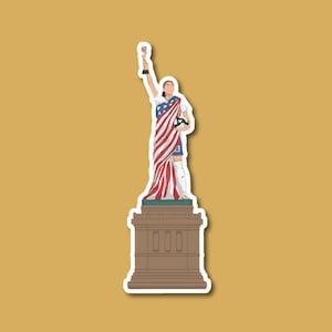 May include: A sticker of a woman holding a soccer ball, standing on a pedestal, with the American flag draped over her. The woman is wearing a white jersey with blue and red accents and the number 3 on the front. The pedestal is brown with three windows.