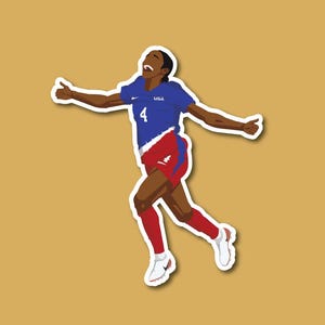 May include: A female soccer player wearing a blue jersey with "USA" and the number "4" on it, red shorts, and white socks, celebrates a goal with her arms raised.