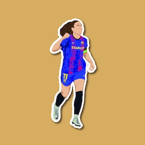 Puede incluir: Una jugadora de fútbol femenino con una camiseta azul y rosa con el texto "STANLEY" en la parte delantera. La camiseta tiene el número "11" en la parte delantera y el logotipo del equipo en el pecho. La jugadora lleva calcetines negros y zapatos blancos y negros.