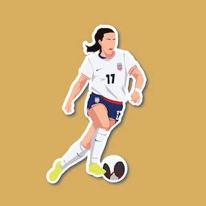 May include: A female soccer player wearing a white jersey with the number 17 and a blue and red USA logo, blue shorts, and white socks, dribbling a soccer ball with her right foot.