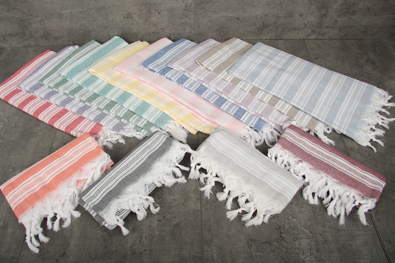 May include: A collection of colorful, striped Turkish towels with fringed edges. The towels are arranged in a fan shape, showcasing a variety of pastel colors including pink, blue, green, and yellow. The towels are made of a lightweight fabric.