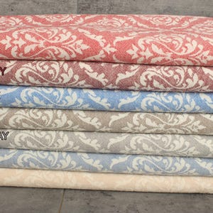 Op de afbeelding: Een stapel van zeven gepatroneerde Turkse handdoeken in verschillende kleuren, waaronder rood, bordeauxrood, blauw, bruin, donkergrijs en beige. De handdoeken hebben een wit damastpatroon en franjes aan de randen.