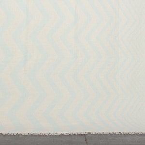 May include: A white throw blanket with a light blue abstract pattern. The blanket has a fringed edge.