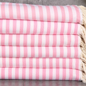 May include: A stack of pink and white striped towels with white fringe. The towels are folded and stacked on a gray surface.