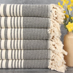 May include: A stack of six white and black striped towels with fringe edges. The towels are folded and stacked on a gray surface.