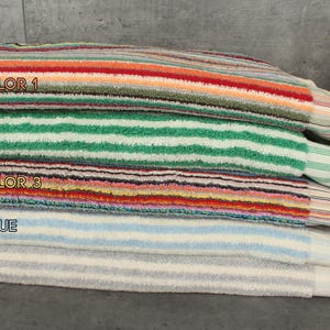 May include: A stack of five striped towels in different colors, including multicolor, green, light blue, and gray. The towels are made of soft, absorbent material and have a fringed edge.