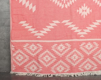 Puede incluir: Una manta de tiro de color rosa y blanco con un borde de flecos. El patrón presenta formas y diseños geométricos.