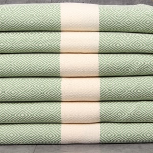 May include: A stack of six green and cream-colored diamond-patterned towels. The towels have a light green diamond pattern with a cream-colored stripe in the middle and cream-colored fringe.
