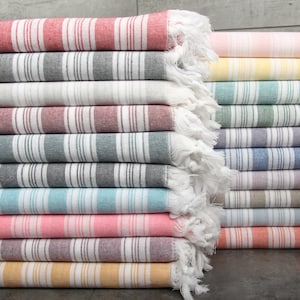 May include: A stack of colorful striped towels. The towels are folded and stacked, showcasing a variety of colors including red, gray, white, pink, yellow, and blue. Each towel has a fringe on one end.