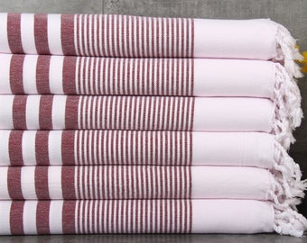May include: A stack of six white and burgundy striped towels. The towels have a fringe on the edge and are folded neatly. The burgundy stripes are vertical and run the length of the towels. The towels are made of a soft, absorbent material.