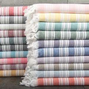May include: A stack of colorful striped Turkish towels. The towels feature vertical stripes in various colors, including red, gray, white, blue, pink, yellow, and orange. Each towel has a fringed edge.