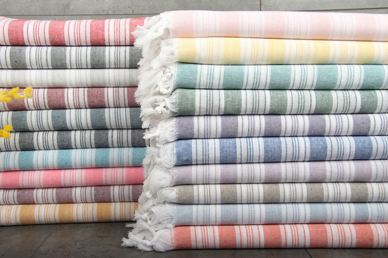 May include: A stack of colorful striped Turkish towels. The towels feature vertical stripes in various colors, including red, gray, white, blue, pink, yellow, and orange. Each towel has a fringed edge.