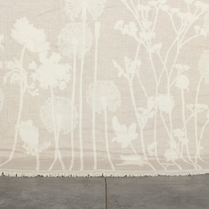 Peut inclure: Une couverture beige avec un motif floral blanc. La couverture a une bordure frangée.