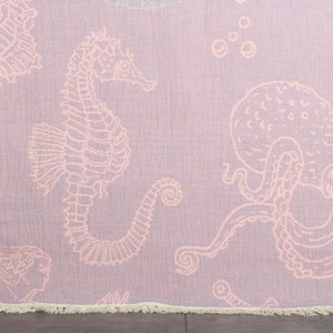 May include: A pink beach towel with a white seahorse and octopus design. The towel has a fringe border.