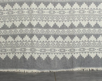 Peut inclure: Une couverture en tissu gris et blanc à motifs avec des franges sur le bord inférieur. Le motif est un design géométrique avec des triangles et des diamants.