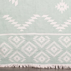 May include: A light green throw blanket with a white geometric pattern. The blanket has a fringe border.