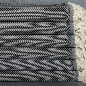 May include: A stack of black and white striped towels with fringed edges. The towels are folded and stacked on a grey surface.