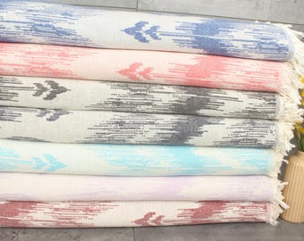 May include: A stack of colorful patterned towels with fringe edges. The towels are folded and stacked on a gray surface.