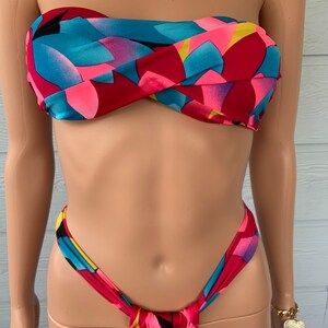 Pu&ograve; includere: Un top e un fondo bikini con motivo rosso, rosa, blu e giallo. Il top &egrave; di stile bandeau senza spalline e il fondo &egrave; di stile a taglio alto.