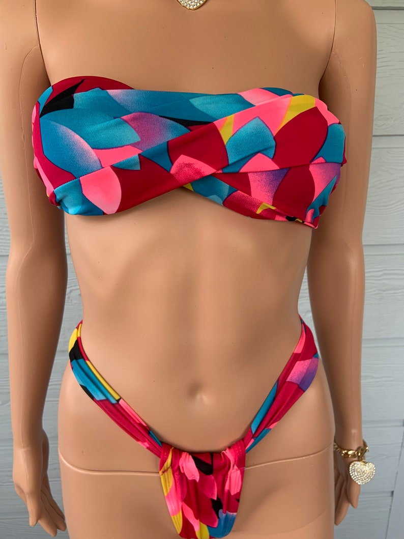 Pu&ograve; includere: Un top e un fondo bikini con motivo rosso, rosa, blu e giallo. Il top &egrave; di stile bandeau senza spalline e il fondo &egrave; di stile a taglio alto.
