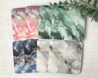 May include: Six decorative coasters with a marble pattern. The coasters are in four different color combinations: pink and gold, green and gold, blue and gold, and gray and gold.