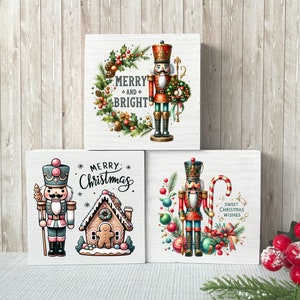 May include: Three square wooden Christmas decorations with festive nutcracker designs and seasonal greetings. One displays "Merry and Bright" with a wreath and nutcracker. Another says "Merry Christmas" with a gingerbread house. The third says "Sweet Christmas Wishes".