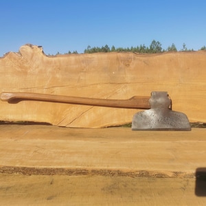 Peut inclure: Une hache vintage avec un manche en bois et une tête en métal, reposant sur une surface en bois. La hache a une lame légèrement incurvée et une tête arrondie.