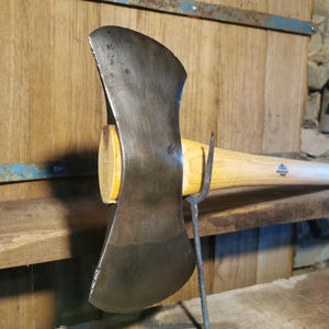 Può includere: Un'ascia a doppia lama con manico in legno. La testa dell'ascia è in acciaio e ha una finitura nera. Il manico è in legno e ha una finitura naturale.