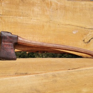 Peut inclure: Une hache vintage avec un manche en bois. La tête de la hache est brun foncé avec de la rouille rouge et le manche est de couleur brun clair.
