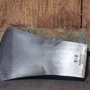 Könnte beinhalten: Ein Vintage-Axtkopf mit silberner Klinge. Der Axtkopf trägt den Text "BRADES CRITERION 312" auf der Seite. Der Hintergrund ist eine Holzoberfläche mit einem rostigen Metallakzent.