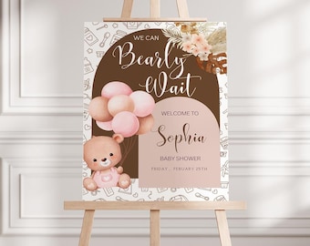May include: A brown and white baby shower welcome sign with the text "We can Bearly Wait" and "Welcome to Sophia Baby Shower Friday, February 25th". The sign features a cartoon bear holding pink balloons and a floral design.