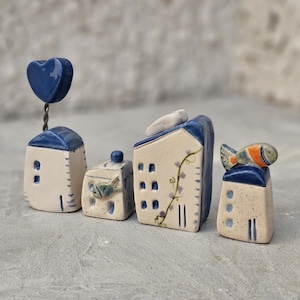 May include: Five miniature ceramic houses with blue and white paint, decorated with floral designs and a small fish. The houses are arranged in a row on a gray surface.