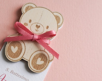 May include: A wooden teddy bear with a pink ribbon, holding a card that says "S. Battesimo Amelia La gioia è più se co".