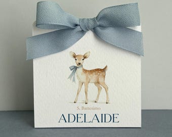 May include: A square white card featuring a watercolor illustration of a fawn wearing a blue ribbon around its neck. The card is topped with a textured dusty blue fabric bow. Below the fawn, the text reads S. Battesimo and ADELAIDE in blue.