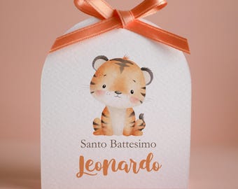 May include: A white arched favor box featuring a watercolor illustration of a seated tiger cub. The box is tied with a peach-colored satin ribbon bow at the top. Text on the front reads Santo Battesimo and the name Jeonardo in orange script.