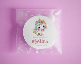 May include: A clear cellophane bag with a white circle sticker featuring a cartoon unicorn with a rainbow mane and tail. The sticker has the text "Santo Battesimo Martina 12 ottobre 2025" in pink and white. The background is a solid light purple.