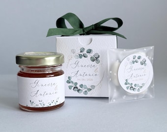May include: A collection of wedding favors includes a small jar of honey, a white gift box with a green ribbon, and a small bag of treats. Each item features a label with the names "Ginevra & Antonio" and the date 14/06/2026.