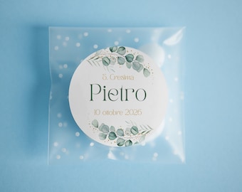 May include: A square translucent pouch with white polka dots containing a round sticker. The sticker features green eucalyptus leaves, gold accents, and the text S. Cresima, Pietro, and 10 ottobre 2026 printed in dark green and gold.